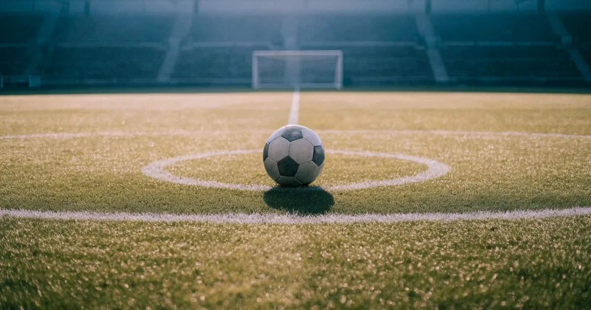 Uma bola de futebol no ponto central de um relvado, à luz da manhã