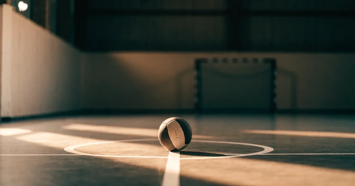 Uma bola de futebol no ponto central de um relvado, à luz da manhã